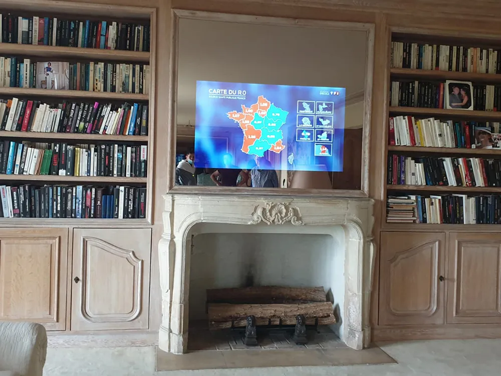Custom installed magic mirror TV above a fireplace in a library