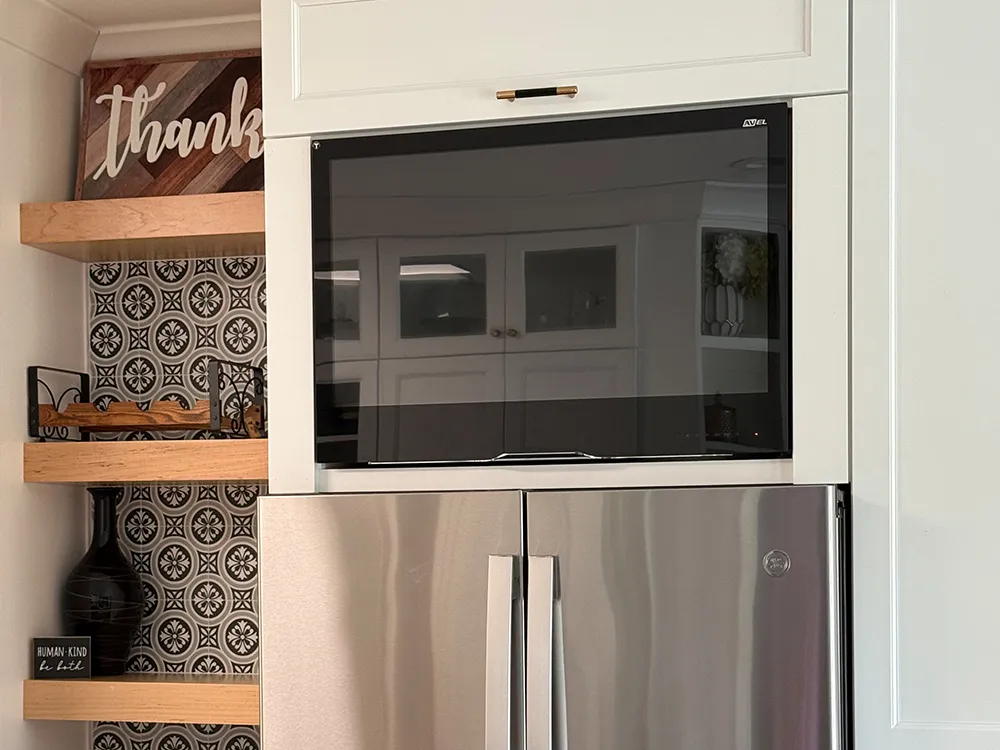 AVEL TV above a refrigerator in a white kitchen with the screen off