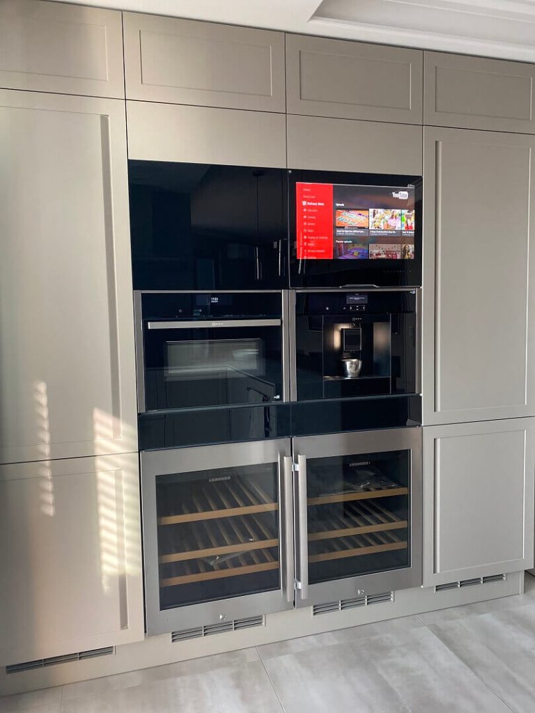 AVEL TV above a coffee machine and wine coolers in a beige kitchen